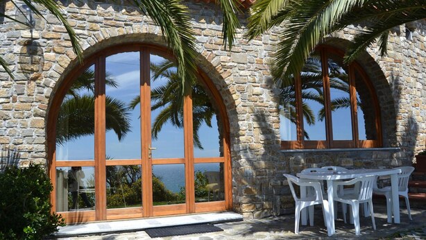 A stone building with large arched windows and a patio area with white plastic chairs.