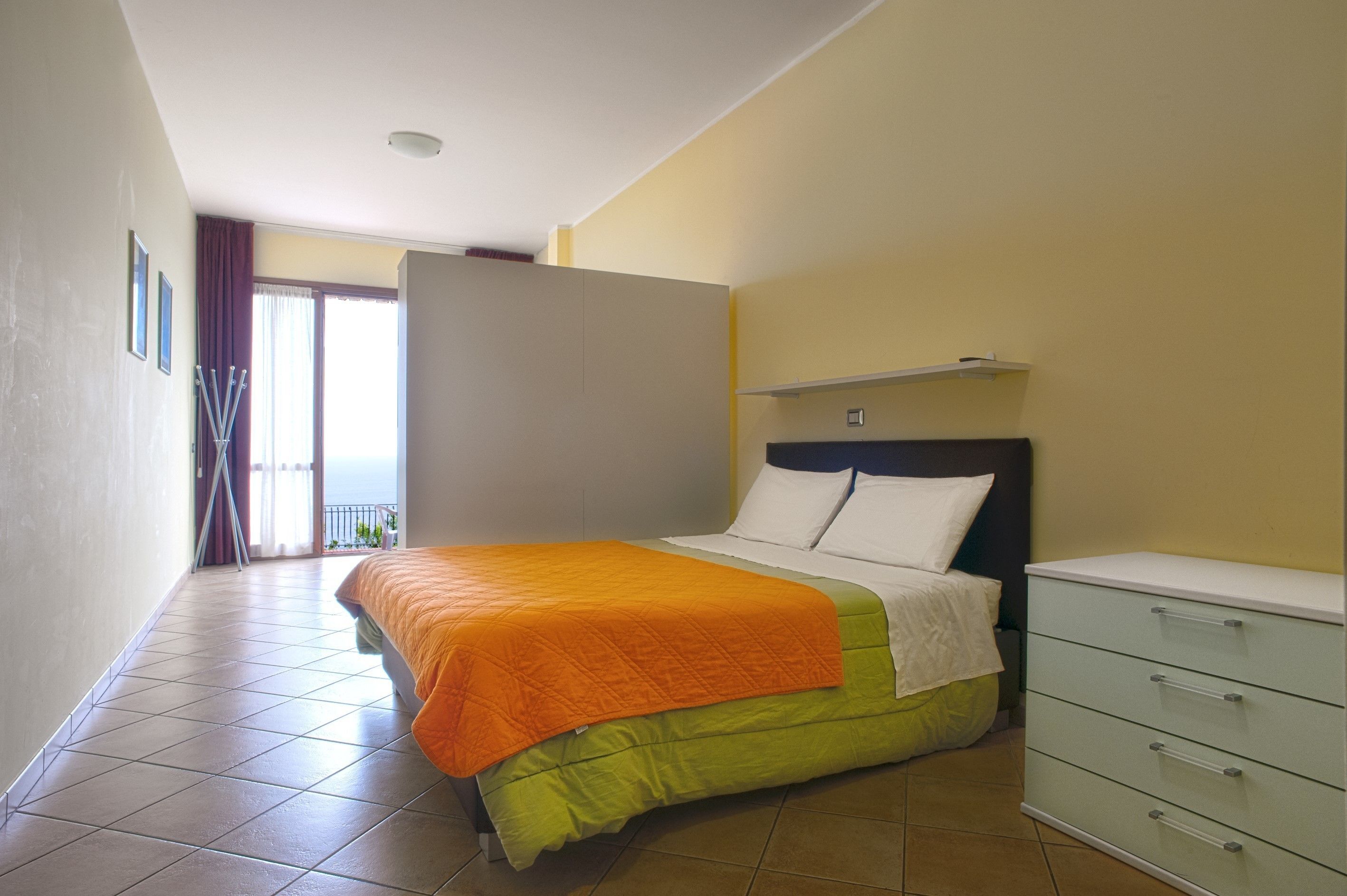 Une chambre à coucher avec un lit, une commode et une porte-fenêtre donnant sur un balcon.