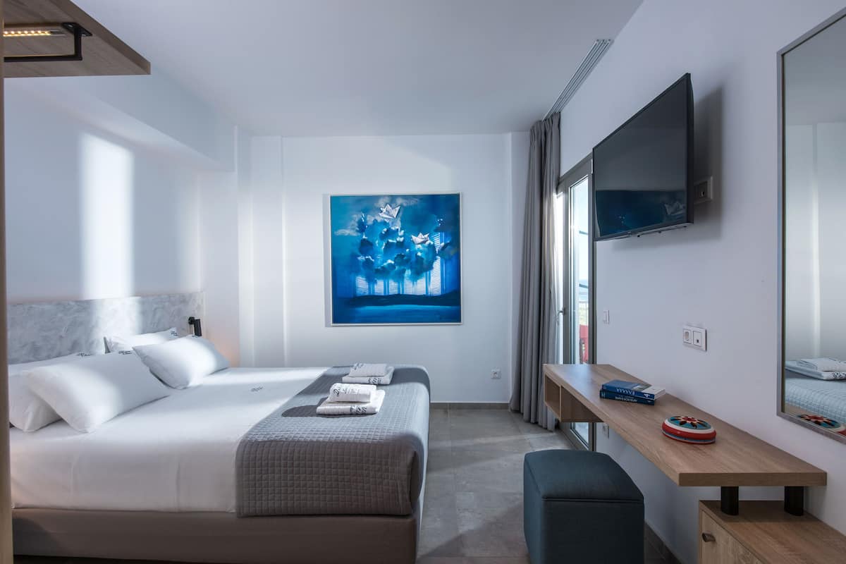 Moderni hotellihuone, jossa on suuri sänky, työpöytä, taulutelevisio ja taulu seinällä.