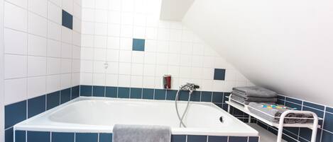 A bathroom with a bathtub, a towel rack, and a shelf with towels.