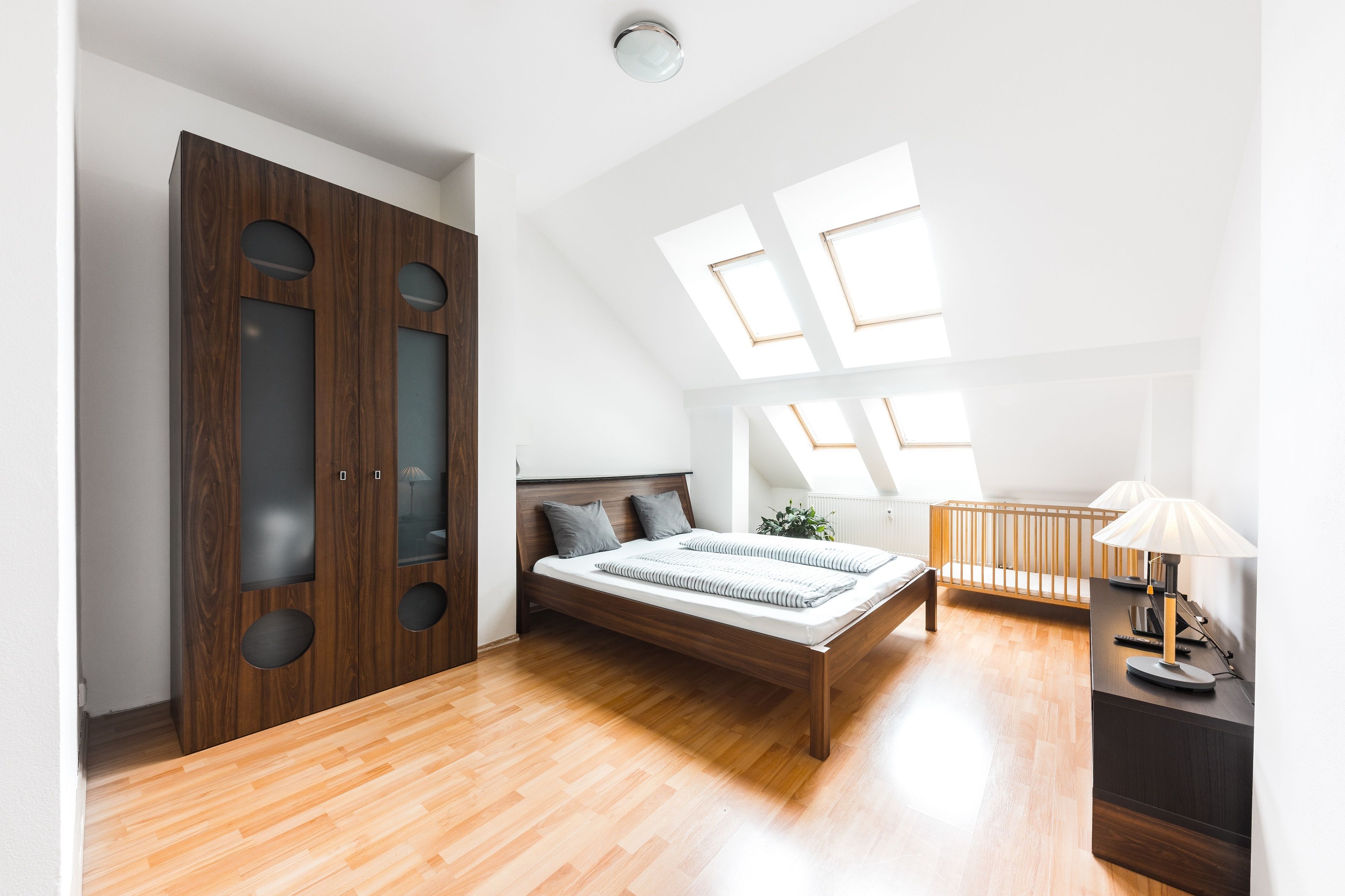 Un dormitorio con una cama de madera, una mesita de noche, una cuna y un armario con detalles circulares.