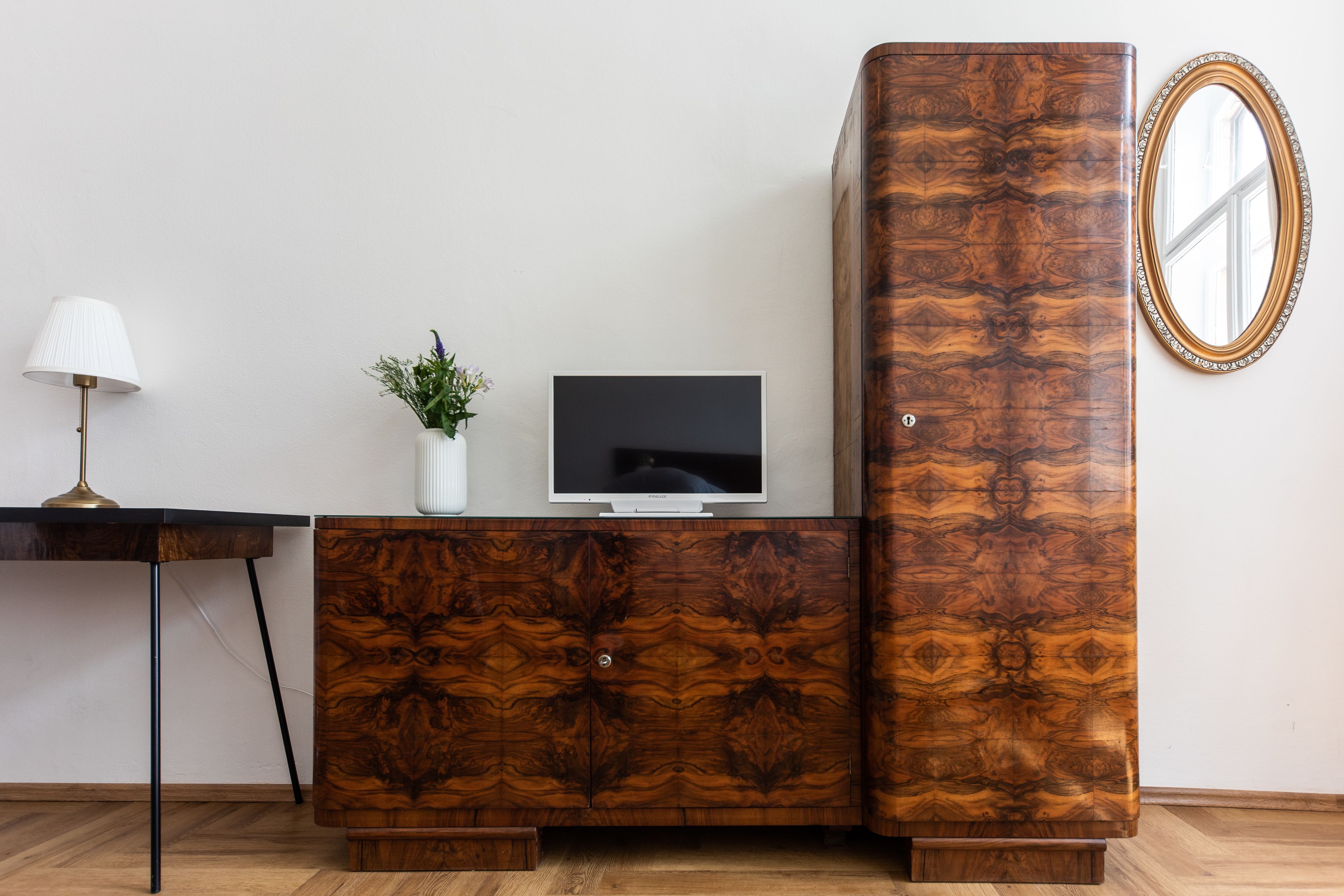A wooden cabinet with a television on top, a small plant, and a lamp on a desk.