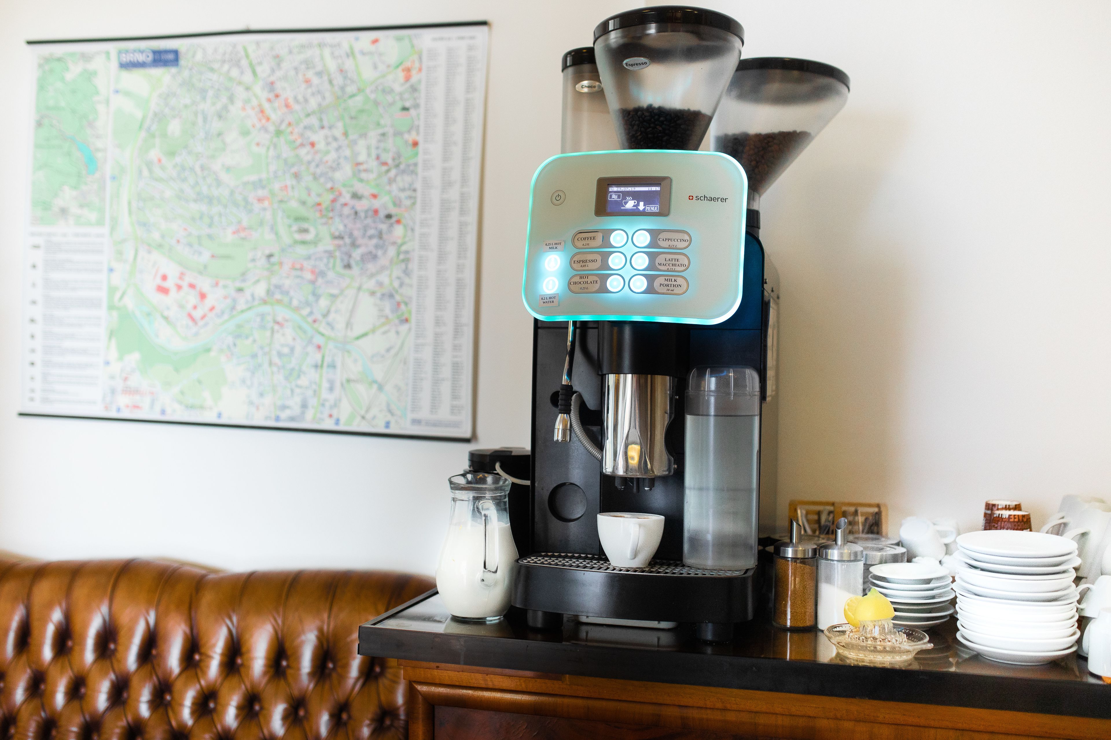 Una máquina de café con pantalla digital, una jarra de leche y una taza de café sobre una encimera.