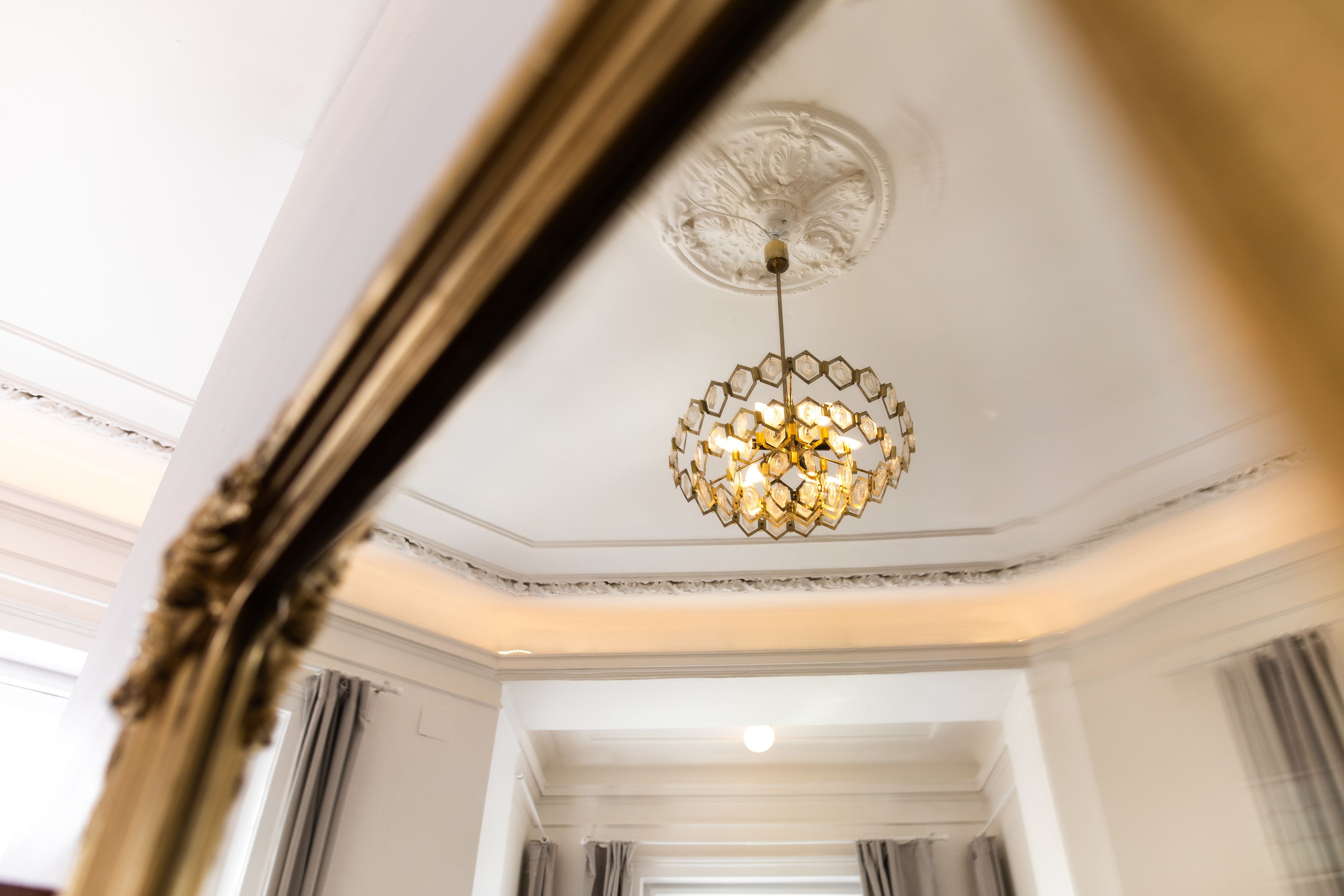 A chandelier with a geometric design hanging from a ceiling with ornate molding.