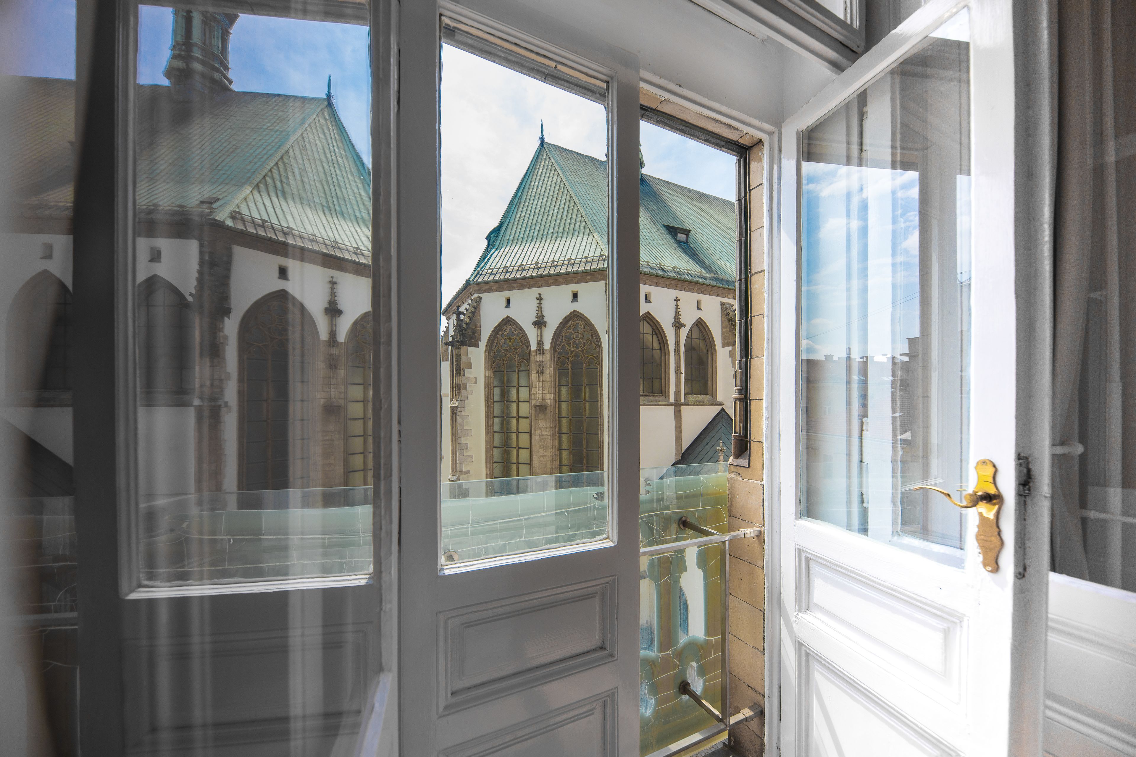 Blick durch eine Glastür mit Metallgriff, der zu einem Gebäude mit Gründach und Rundbogenfenstern führt.