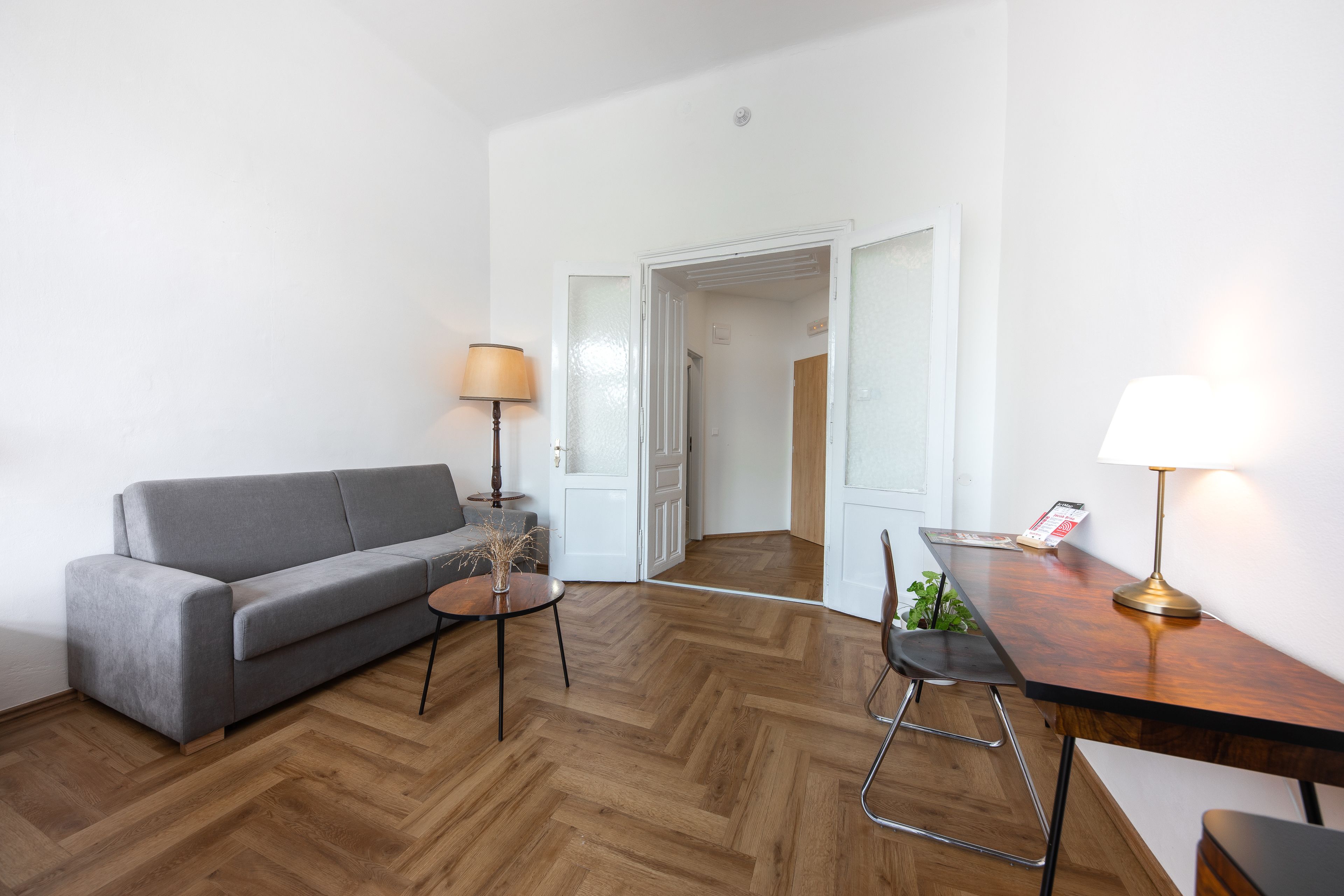 A modern living room with a grey sofa, a wooden coffee table, a lamp, and a wooden desk with a chair.