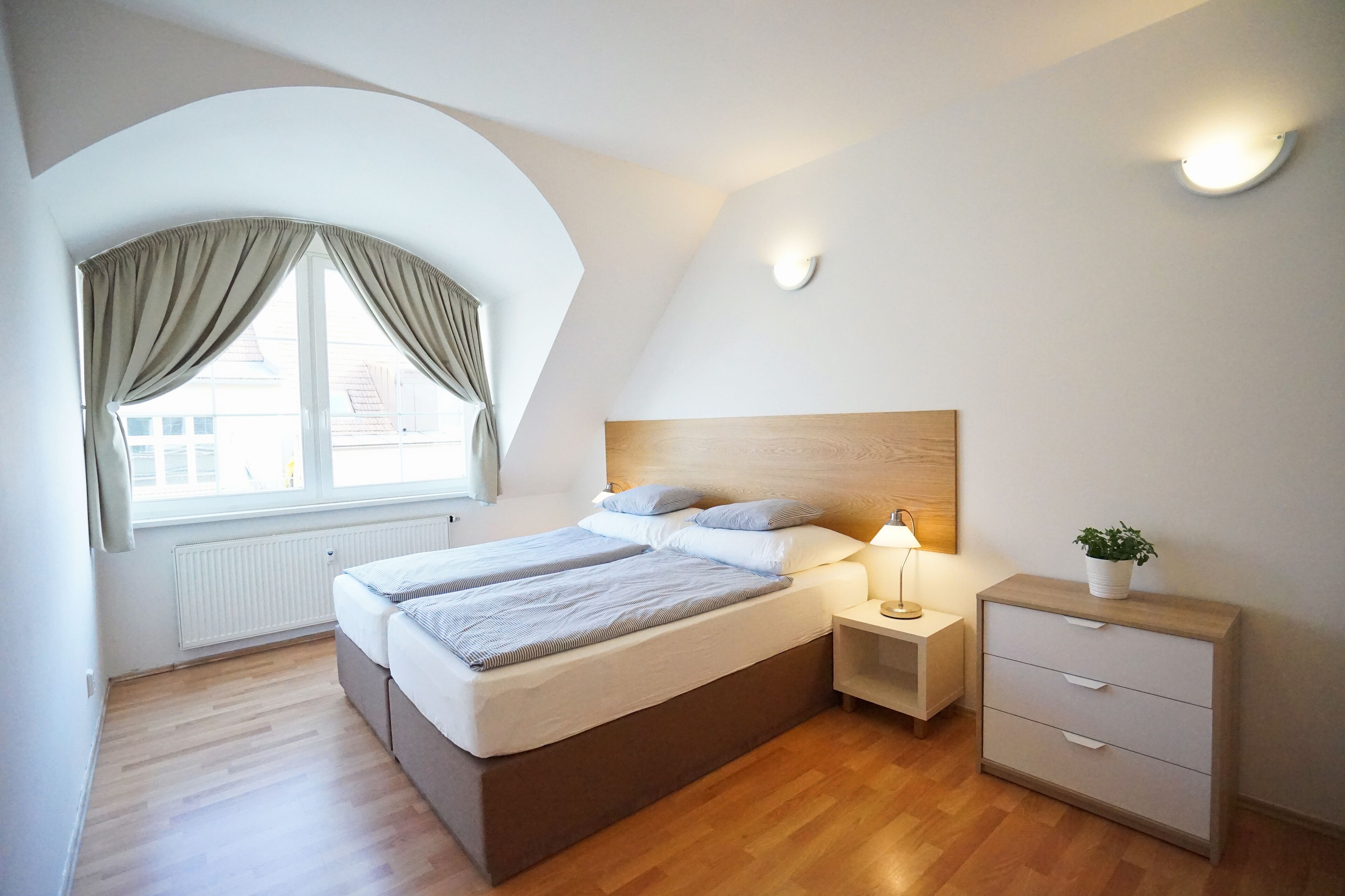 A bedroom with a bed, bedside tables, a nightstand, and a window with curtains.