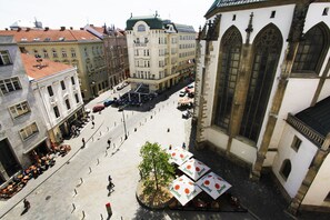 Un espacio cuadrado con mesas al aire libre, rodeado de edificios históricos con ventanas arqueadas y un árbol en el centro.