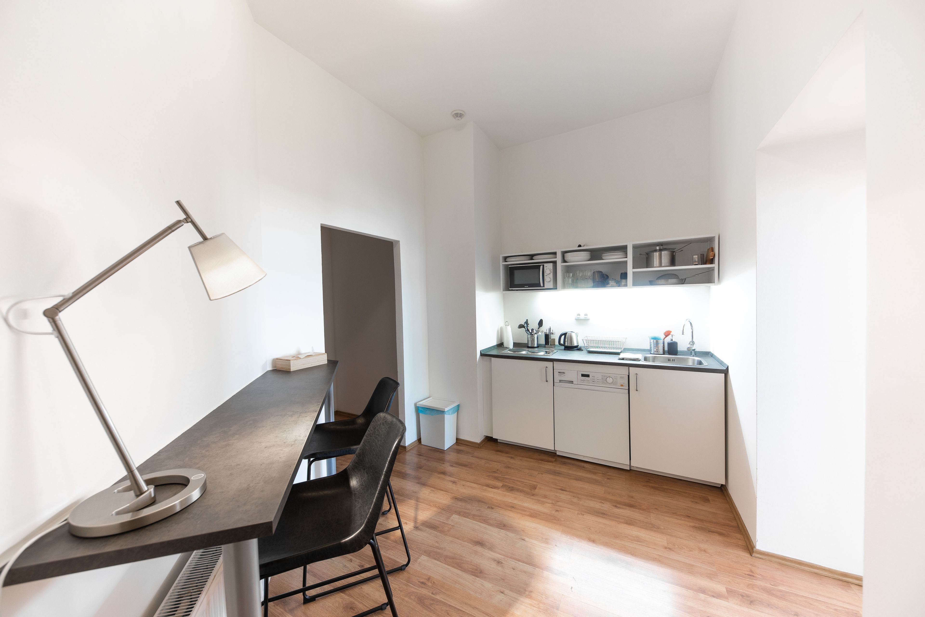 Una cocina moderna con armarios blancos, un microondas y un lavamanos. Hay un comedor con una mesa y sillas.