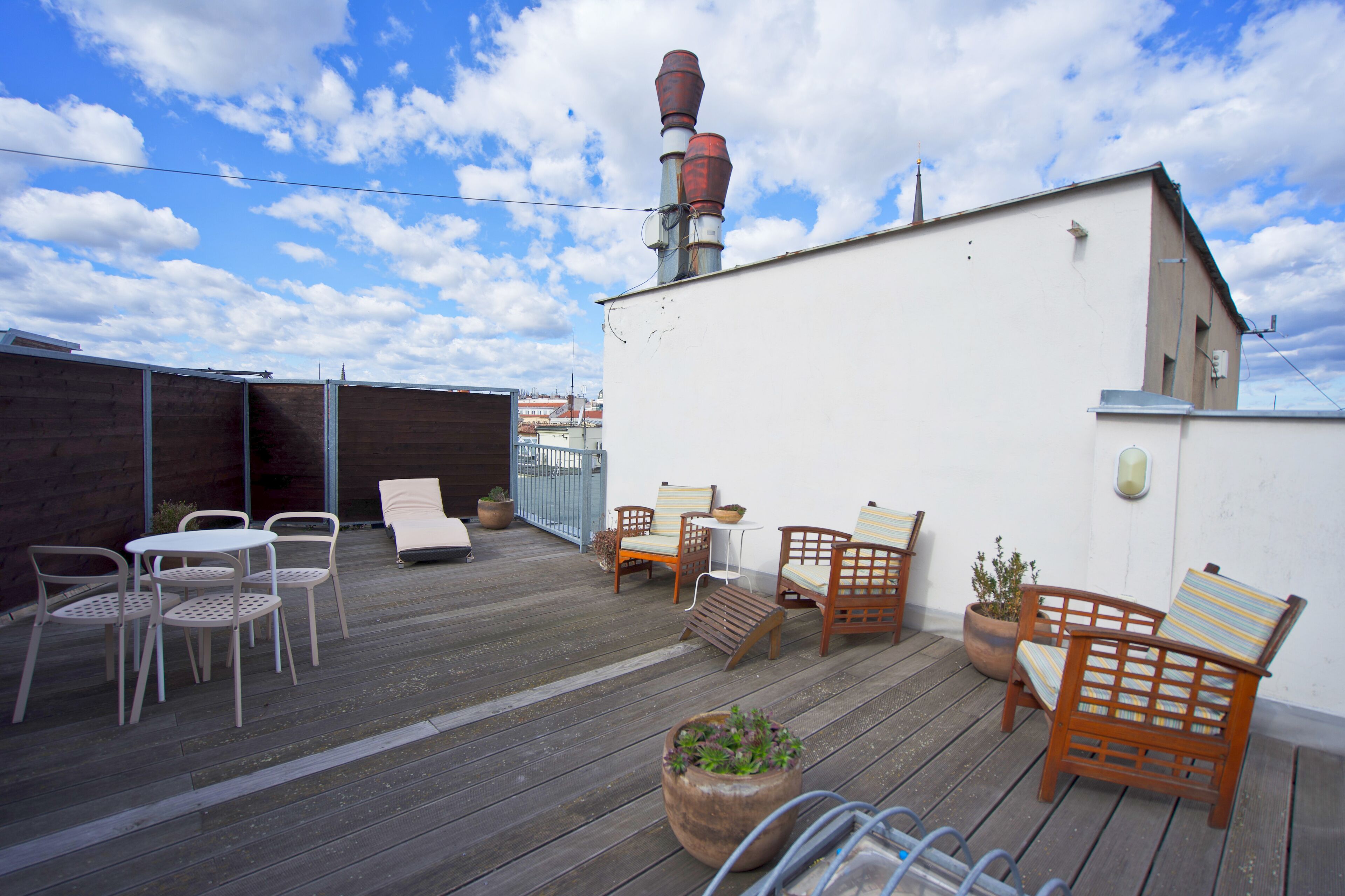 Una terraza en la azotea con mobiliario exterior, una cubierta de madera y un edificio blanco al fondo.
