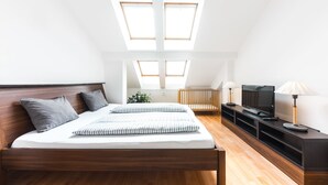 A bedroom with a wooden bed, two skylights, a TV, and a console table with lamps. - Hotel and Apartments Jacob (Brno)