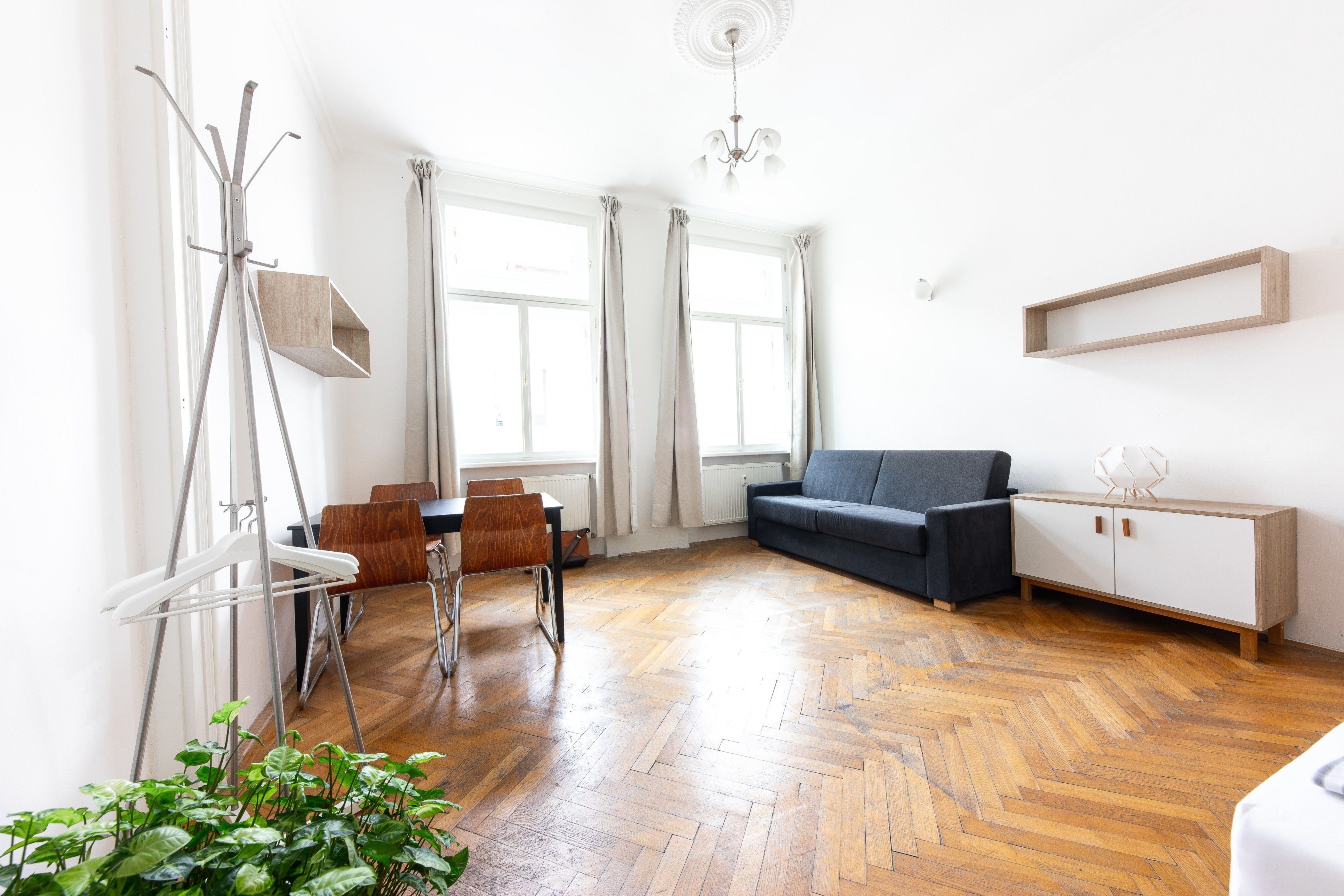 Una sala de estar moderna con piso de madera tipo espiga, un sofá gris, un mueble blanco y un área de comedor con mesa y sillas.