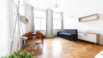 Una sala de estar moderna con piso de madera tipo espiga, un sofá gris, un mueble blanco y un área de comedor con mesa y sillas.