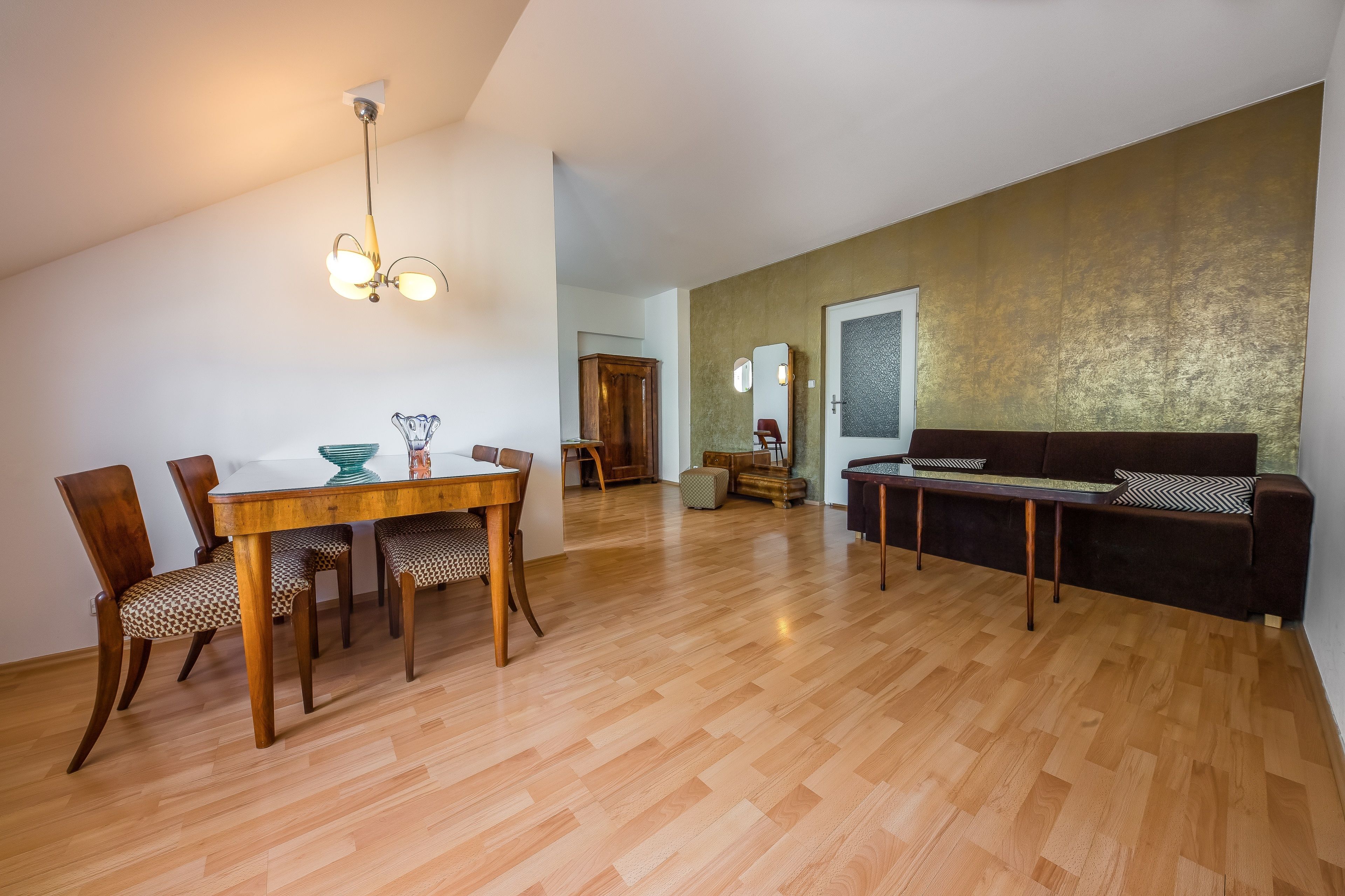 A spacious living area with a wooden floor, a dining table with chairs, a sofa, and a ceiling light fixture.