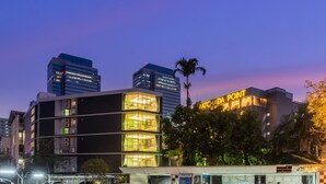 A modern hotel with a prominent sign, surrounded by high-rise buildings and palm trees. - Ratchada Point Hotel (Bangkok)