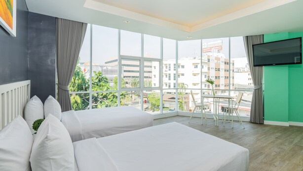 A hotel room with two beds, a large window with a view of buildings, a TV on the wall, and a small table with chairs. - Ratchada Point Hotel (Bangkok)