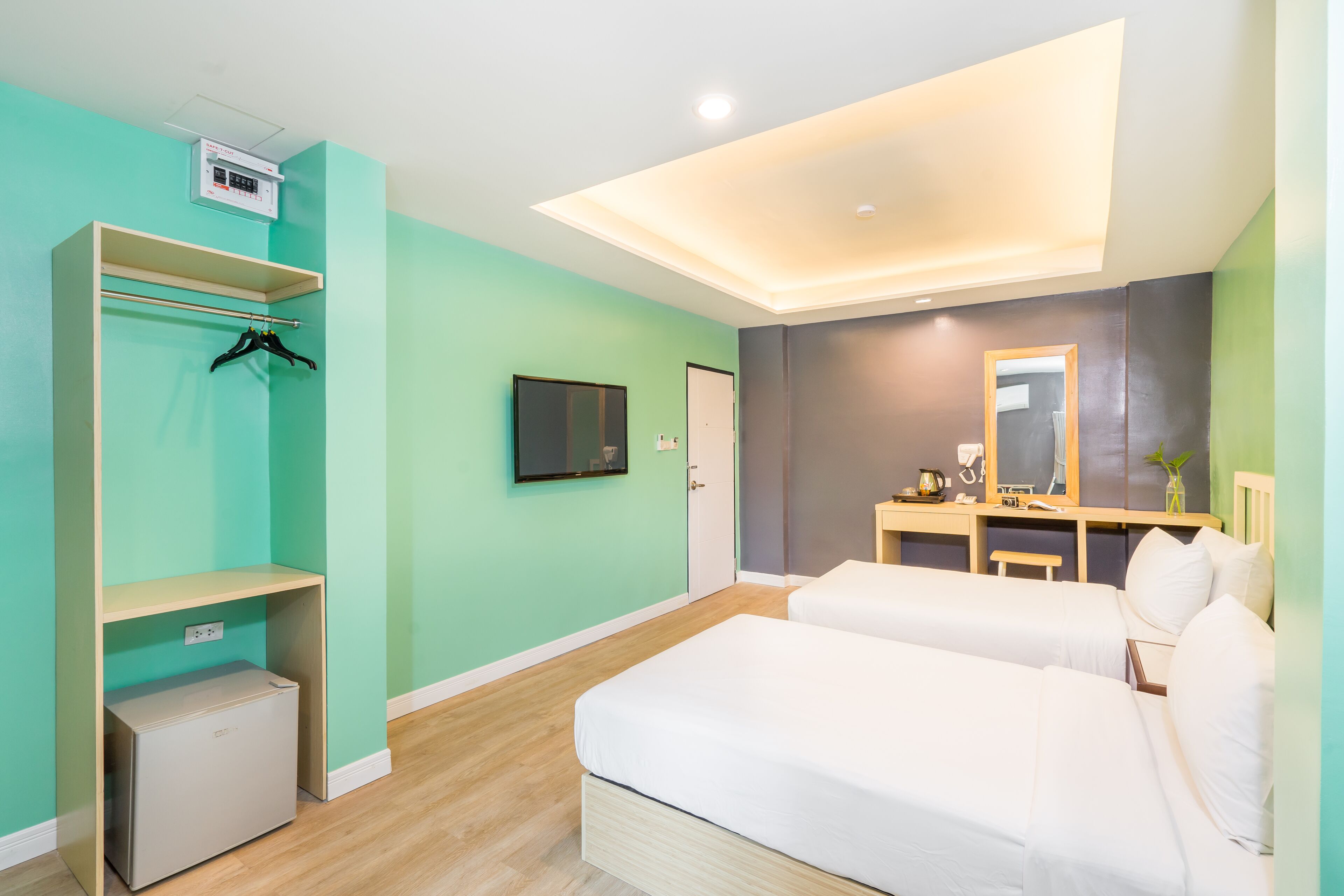 Une chambre d’hôtel moderne équipée de deux lits, d’une télévision, d’un bureau avec un miroir et d’une armoire avec une tringle pour suspendre les vêtements.