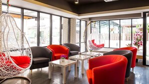 A modern interior with hanging chairs, sofas, and tables, large windows, and a brick wall. - Ratchada Point Hotel (Bangkok)