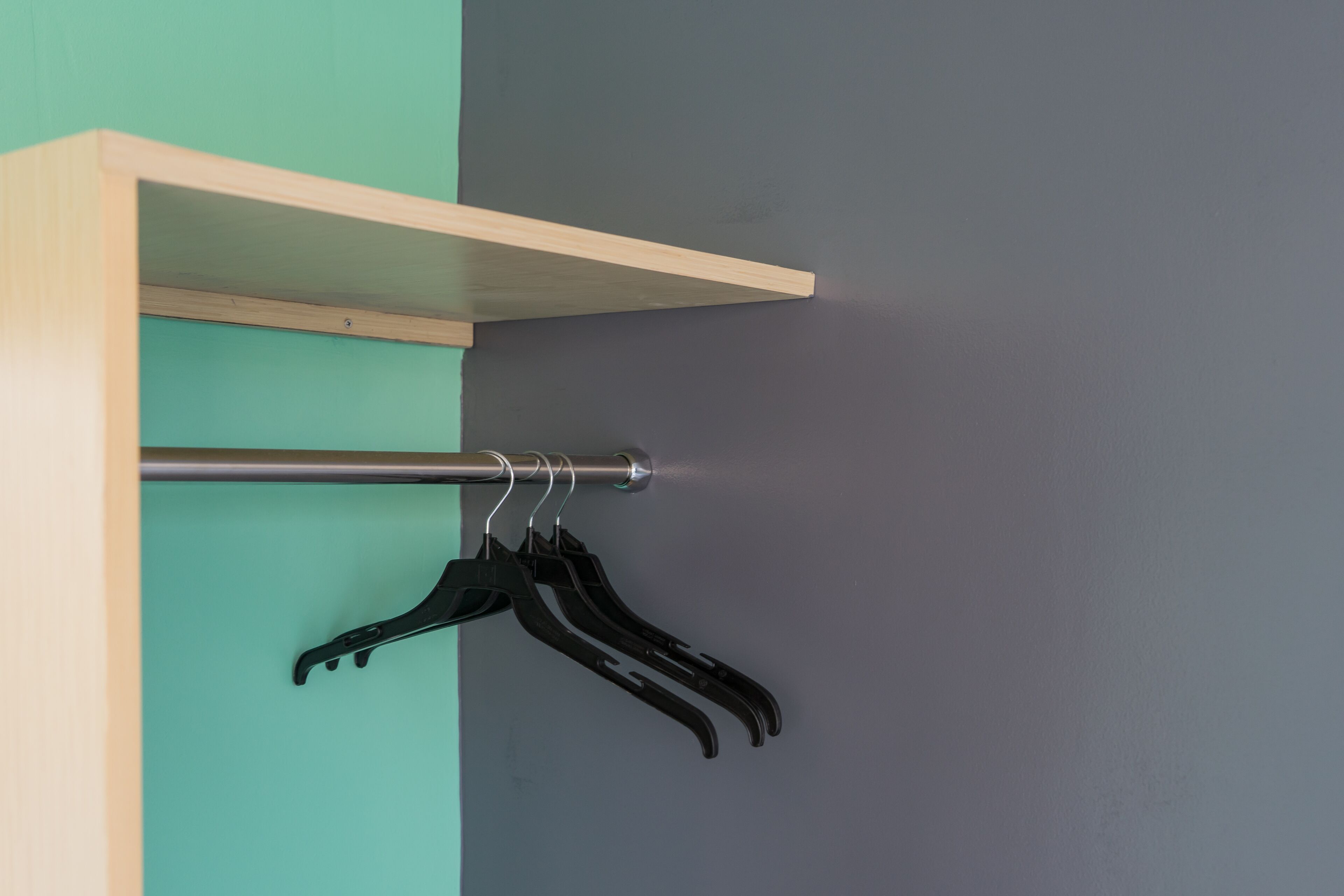 Een wandrek met een metalen stang en zwarte ophanghaakjes tegen een muur in teal en grijs.