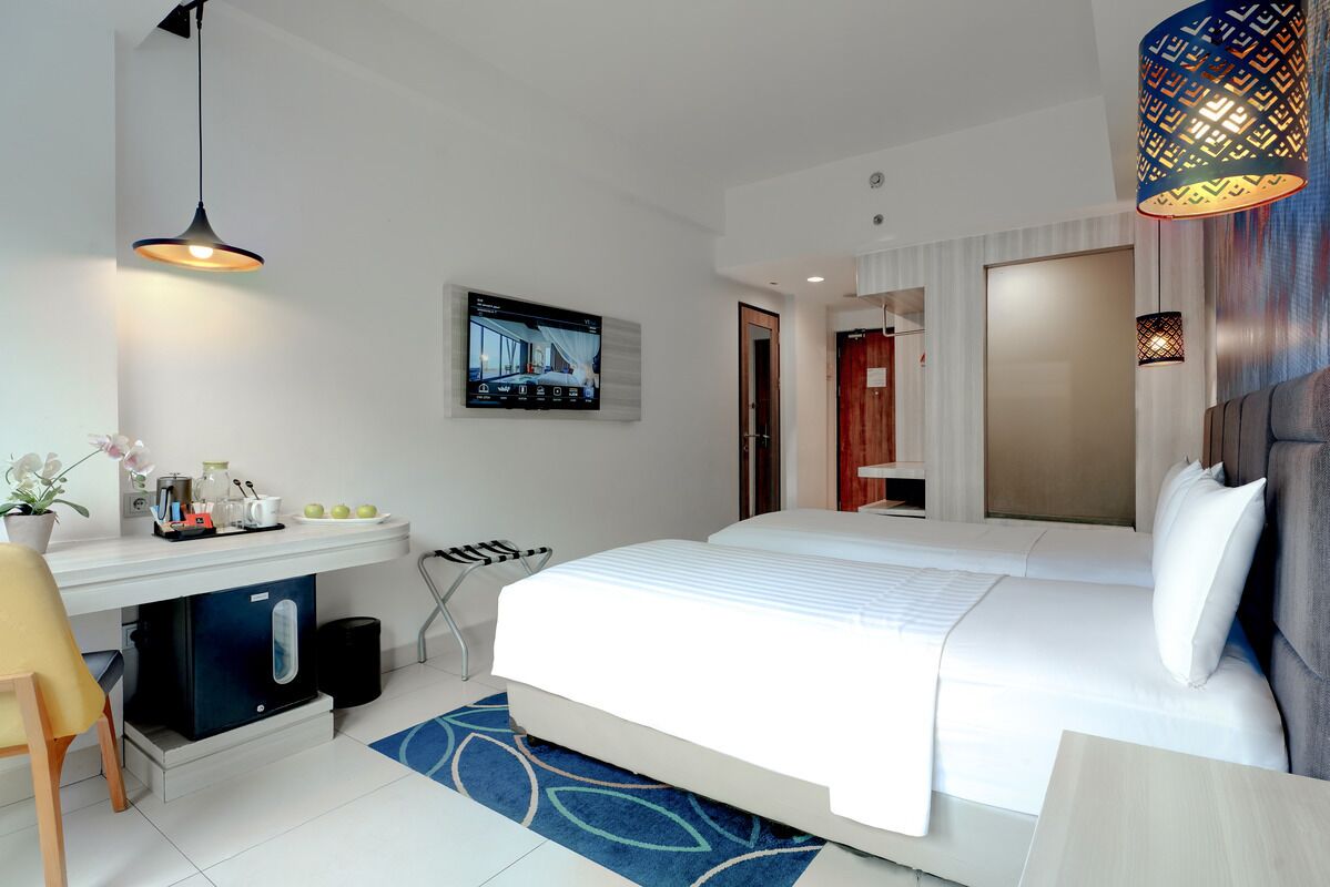 Una habitación de hotel moderna con una cama grande, un escritorio con cafetera, un televisor montado en la pared y una alfombra estampada.