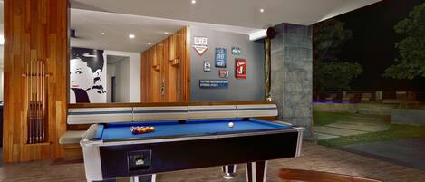 A pool table with a blue felt surface, surrounded by wooden chairs and a table.