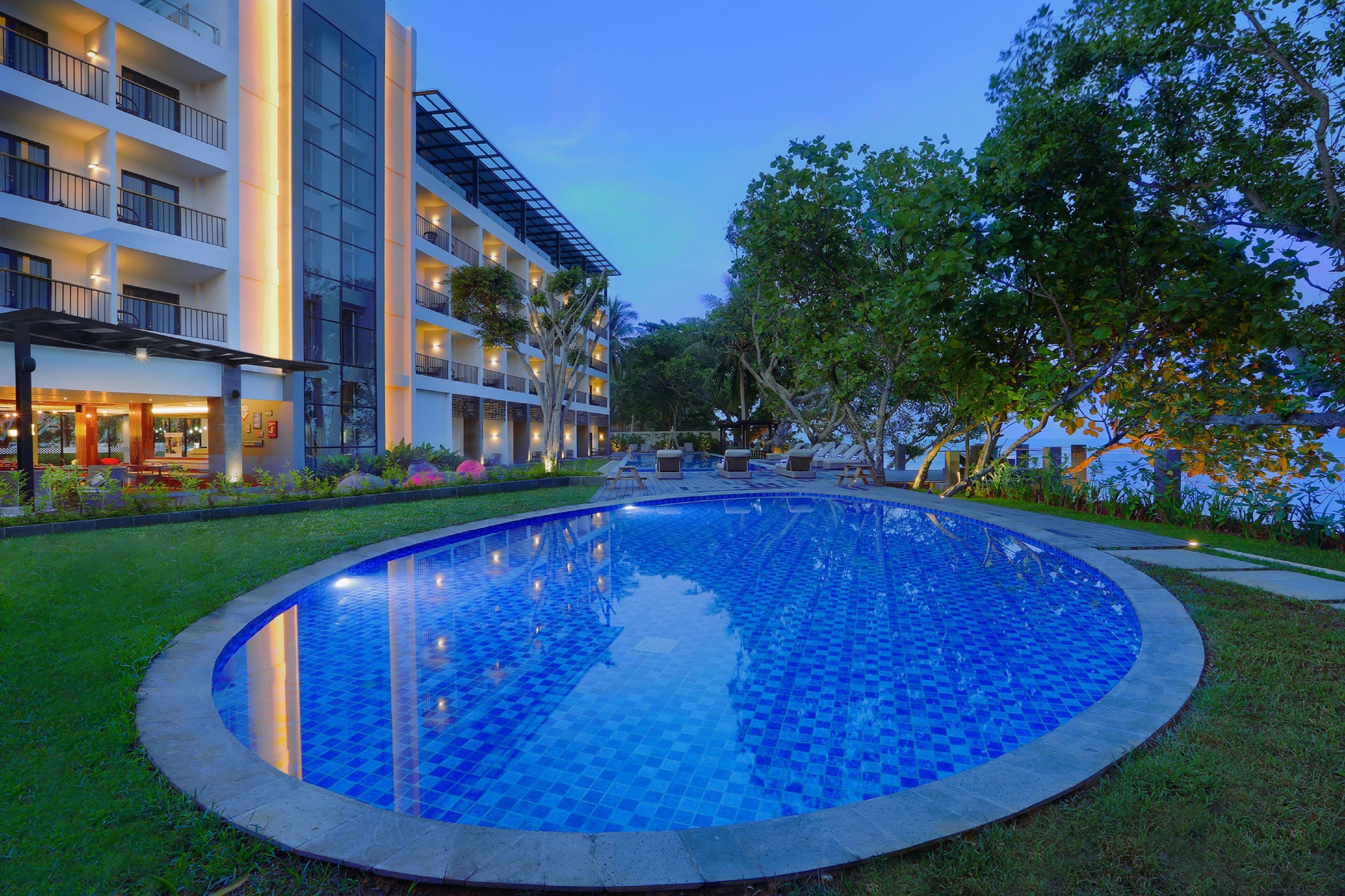 Ein modernes Hotel mit einem runden Pool, mehreren Balkonen und üppiger Bepflanzung.