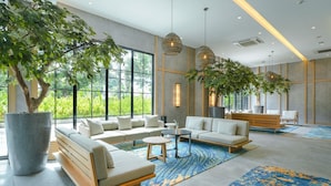 Un hall d’hôtel moderne, agrémenté d’un grand arbre en pot, d’un ensemble de canapés, d’une table basse et de luminaires suspendus.