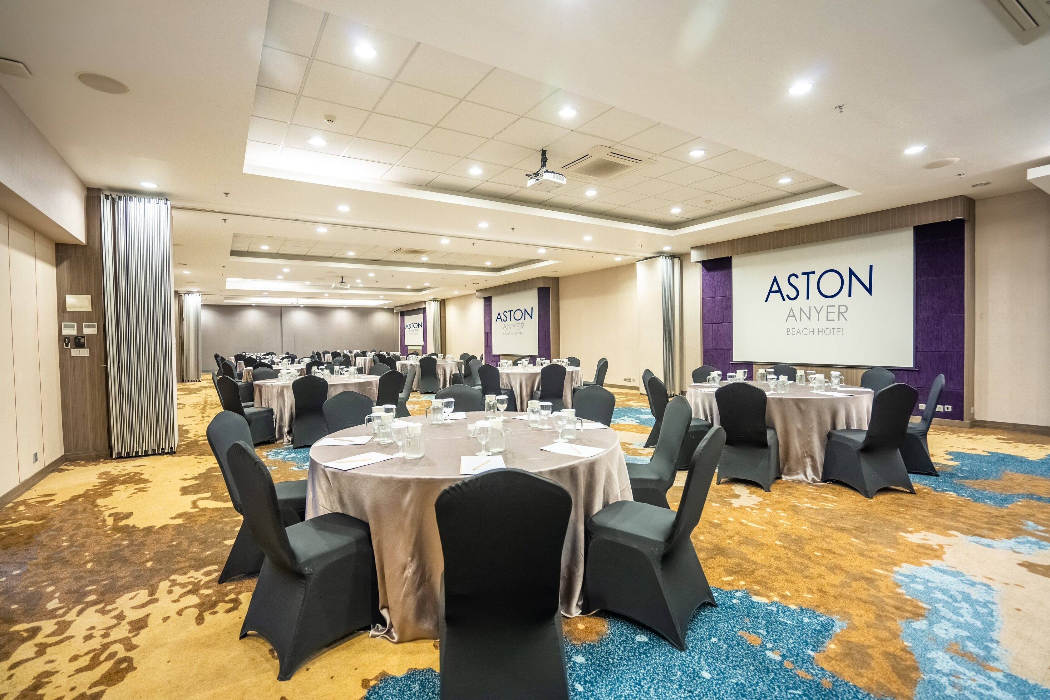 A conference room with round tables, black chairs, and a carpeted floor.