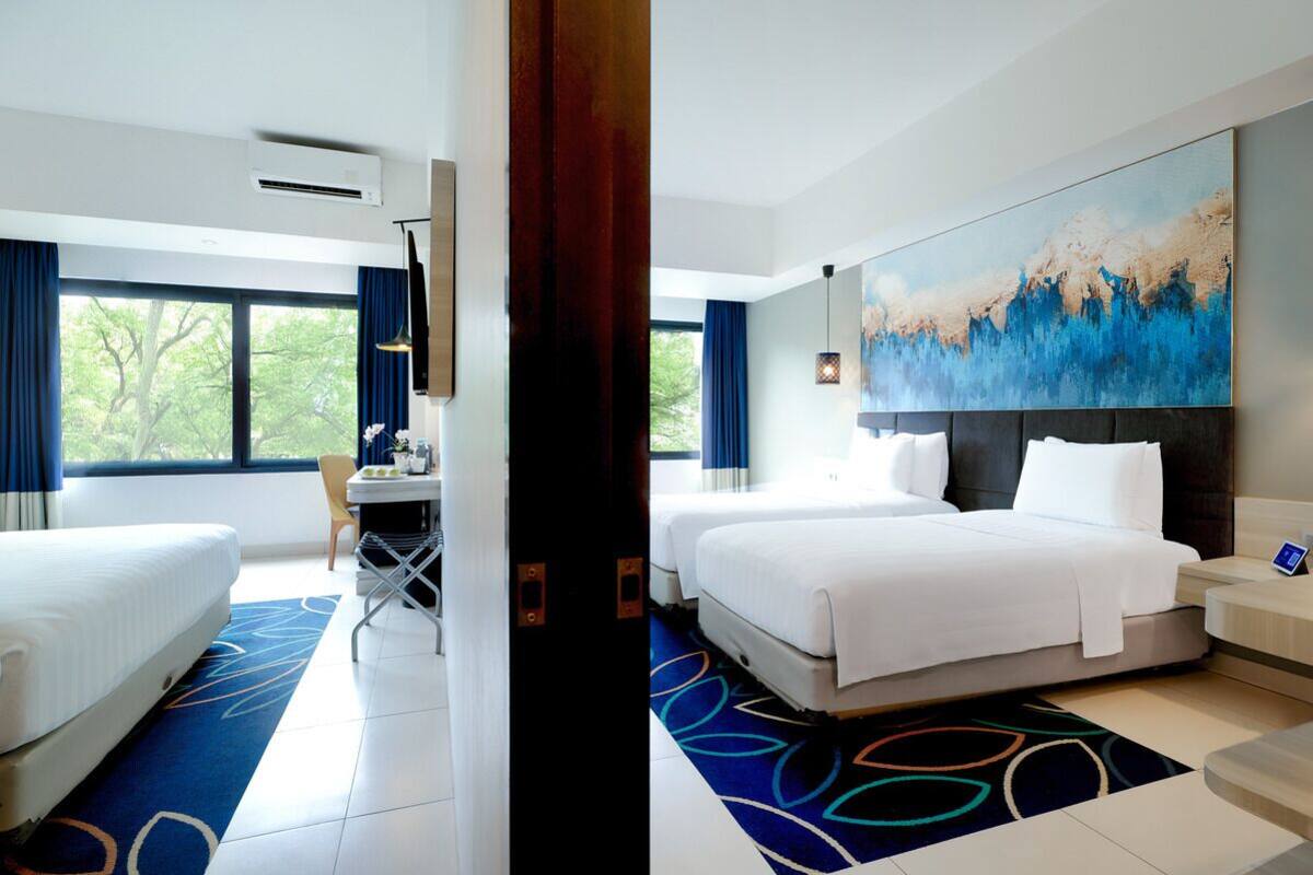 Une chambre d’hôtel avec deux lits, un bureau et une grande fenêtre donnant sur la verdure.
