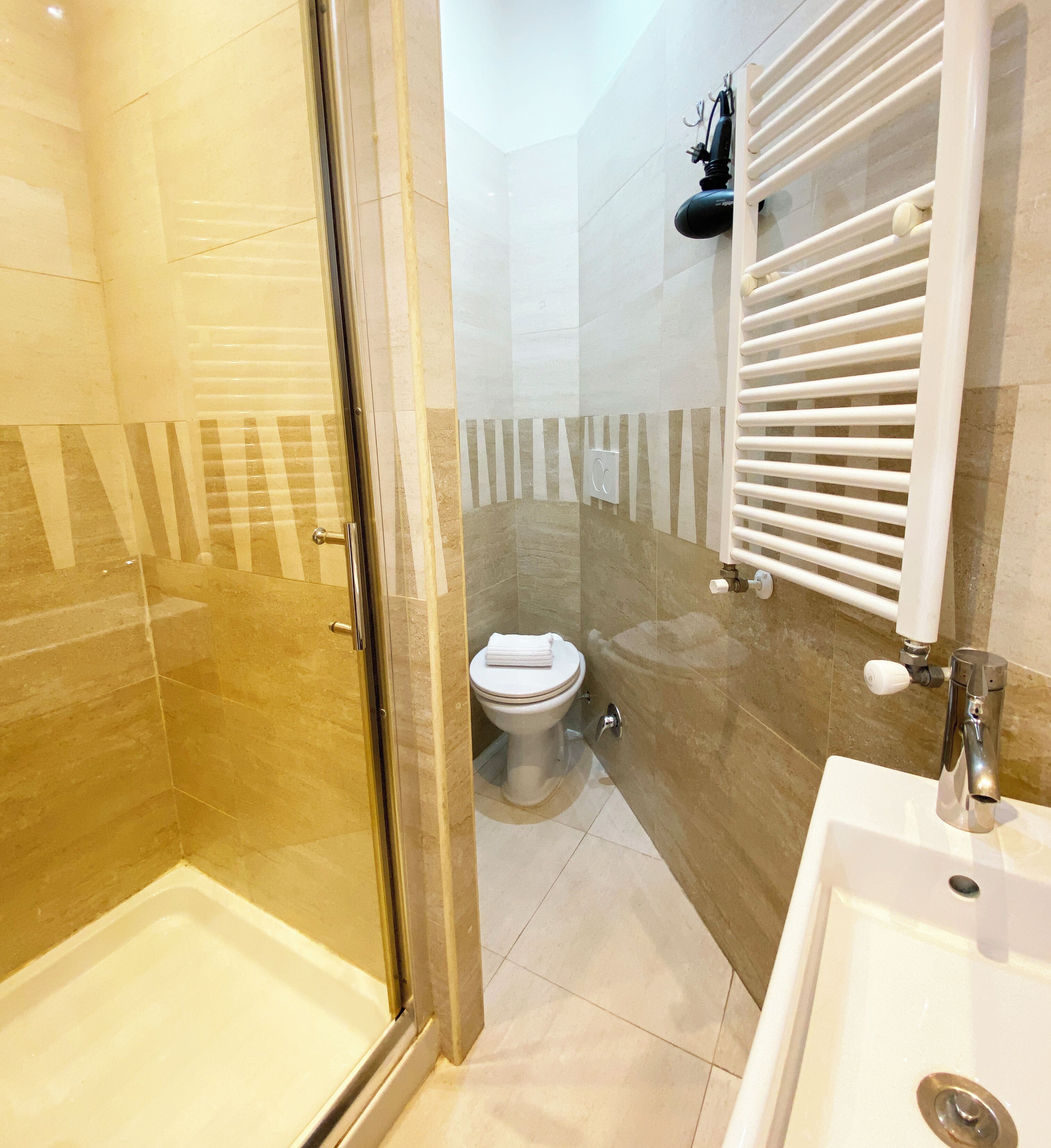 Un baño con cabina de ducha de vidrio, inodoro, lavabo y perchero para toallas.