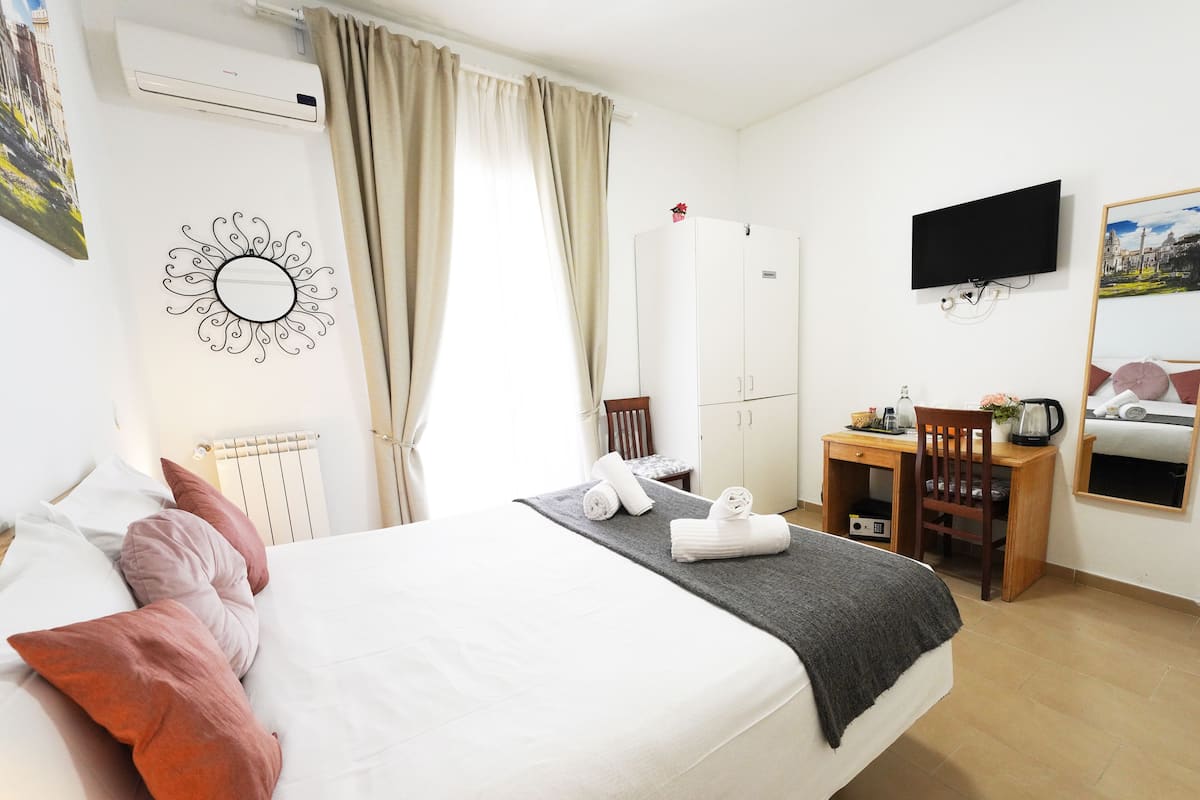 A hotel room with a bed, a desk, a chair, a TV, and a wardrobe.