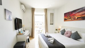 Ett hotellrum med en säng, ett nattduksbord, en tv, ett skrivbord, en stol och en tavla som föreställer en solnedgång.