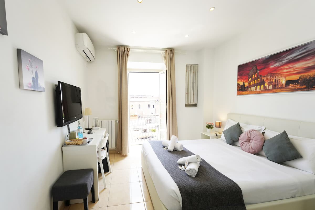 A hotel room with a bed, bedside table, TV, desk, chair, and a painting of a sunset.