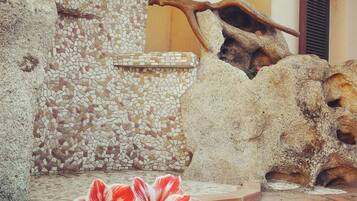 Eine Steinsäule mit Mosaikfliesen, eine große Felsformation und eine rote Blume im Vordergrund.