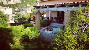 A house with a stone facade, a tiled roof, and a garden with various plants and flowers.