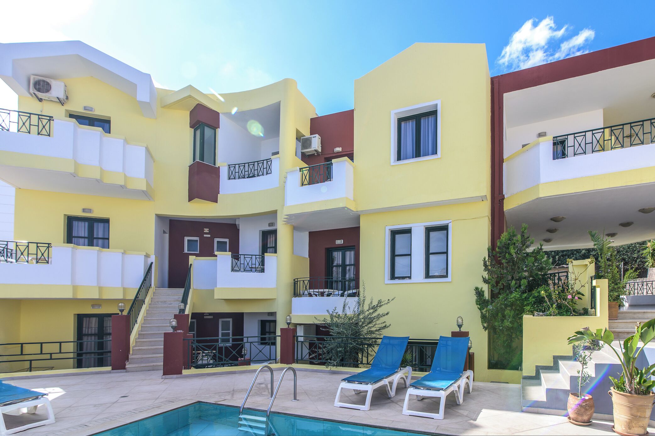 Un edificio de varios pisos con un área de piscina, que incluye una escalera, sillones de descanso y plantas en macetas.