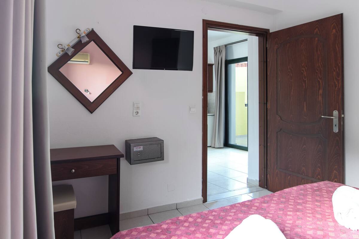Een hotelkamer met een bed, een bureau, een aan de muur bevestigde televisie, een deur en een raam.