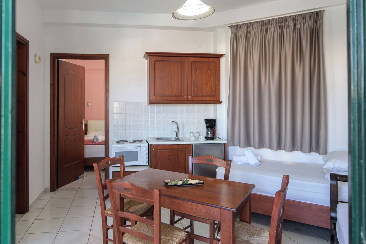 Een kleine hotelkamer met een kitchenette, een eethoek en een bed.
