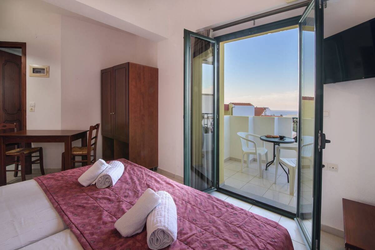 Een hotelkamer met een bed, een bureau en een stoel. Er is een balkon met een tafel en stoelen.