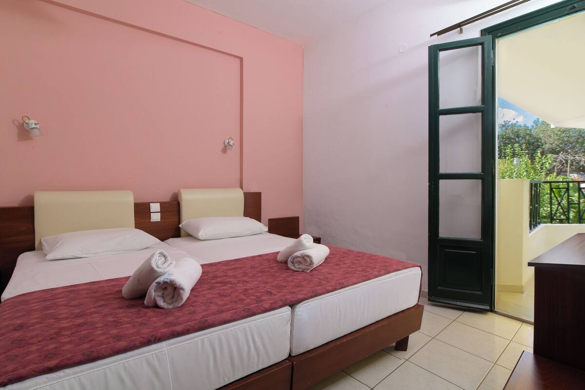 Een hotelkamer met twee bedden, een balkon met uitzicht en een deur naar buiten.