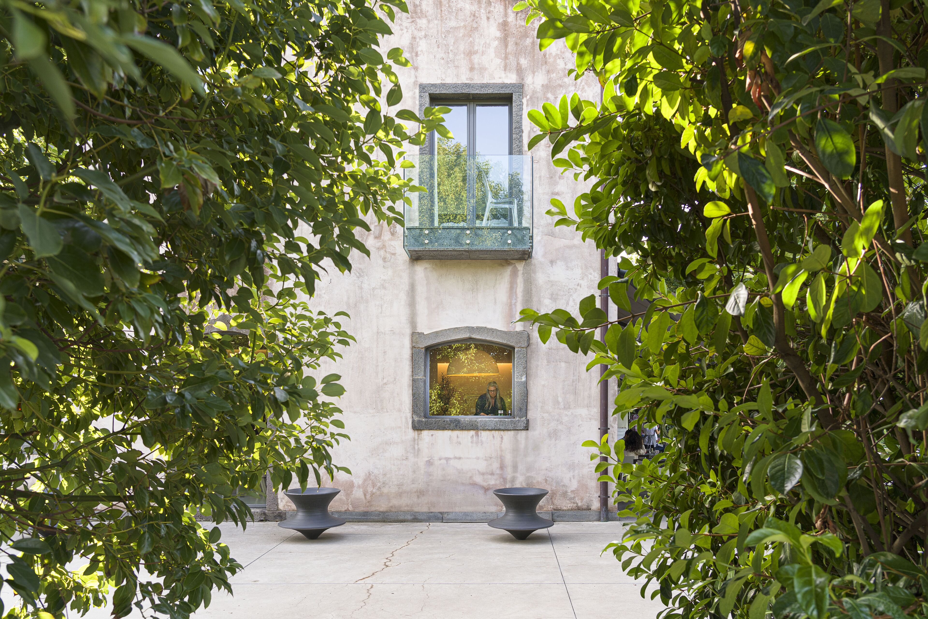 A courtyard with a building, two large planters, and a window with a view.