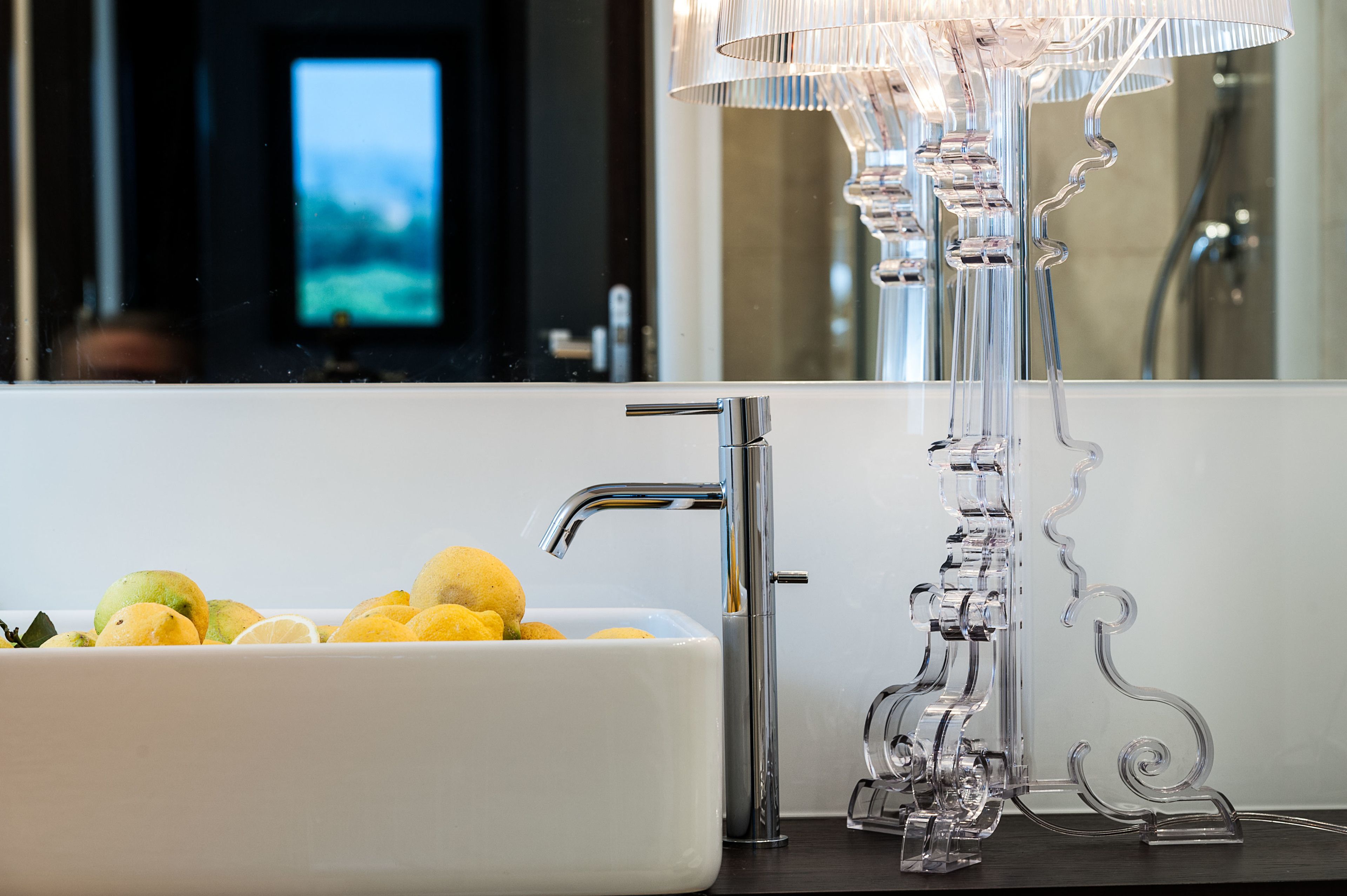 A modern bathroom with a white sink, a chrome faucet, and a clear, decorative glass lamp.