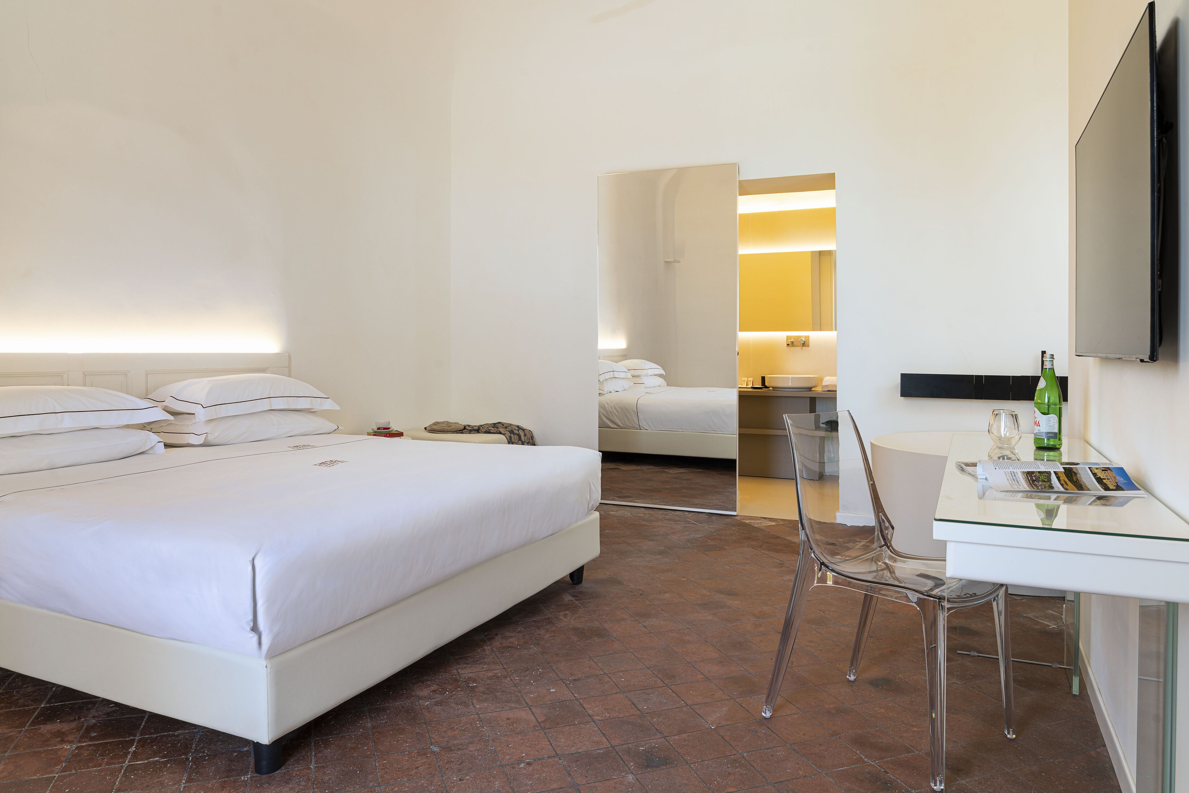 A hotel room with a large bed, a desk, a chair, and a television on the wall.
