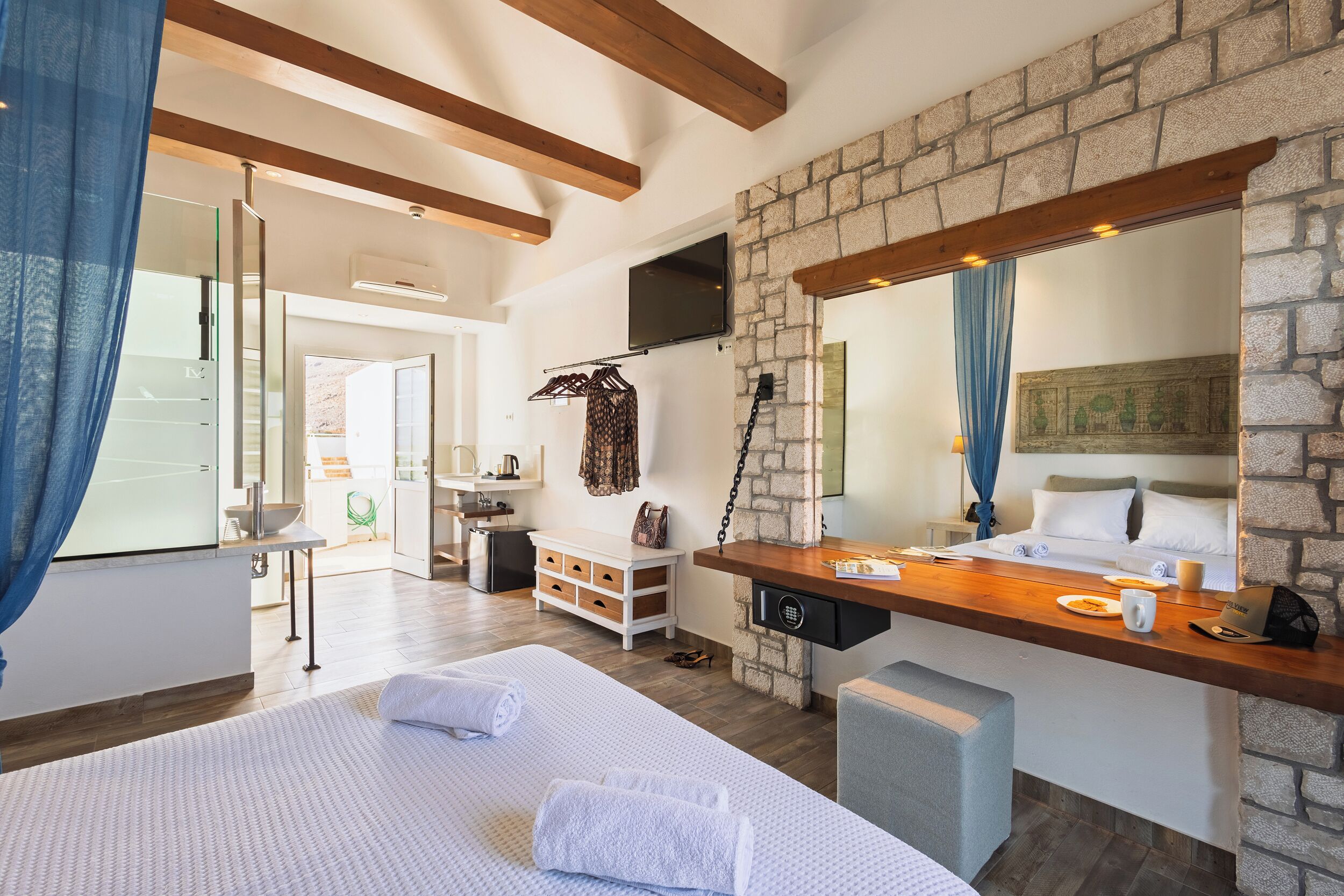 Una camera d'albergo moderna con un letto grande, una panca in legno, un muro in pietra e un televisore sopra un camino.