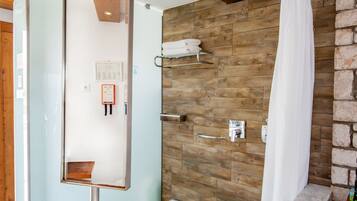 A bathroom with a large mirror, a sink, a shower, and a wooden wall.