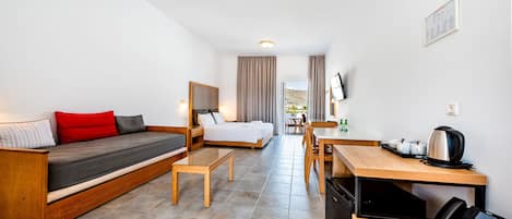 A modern hotel room with a bed, a sofa, a dining table, and a kitchen area.