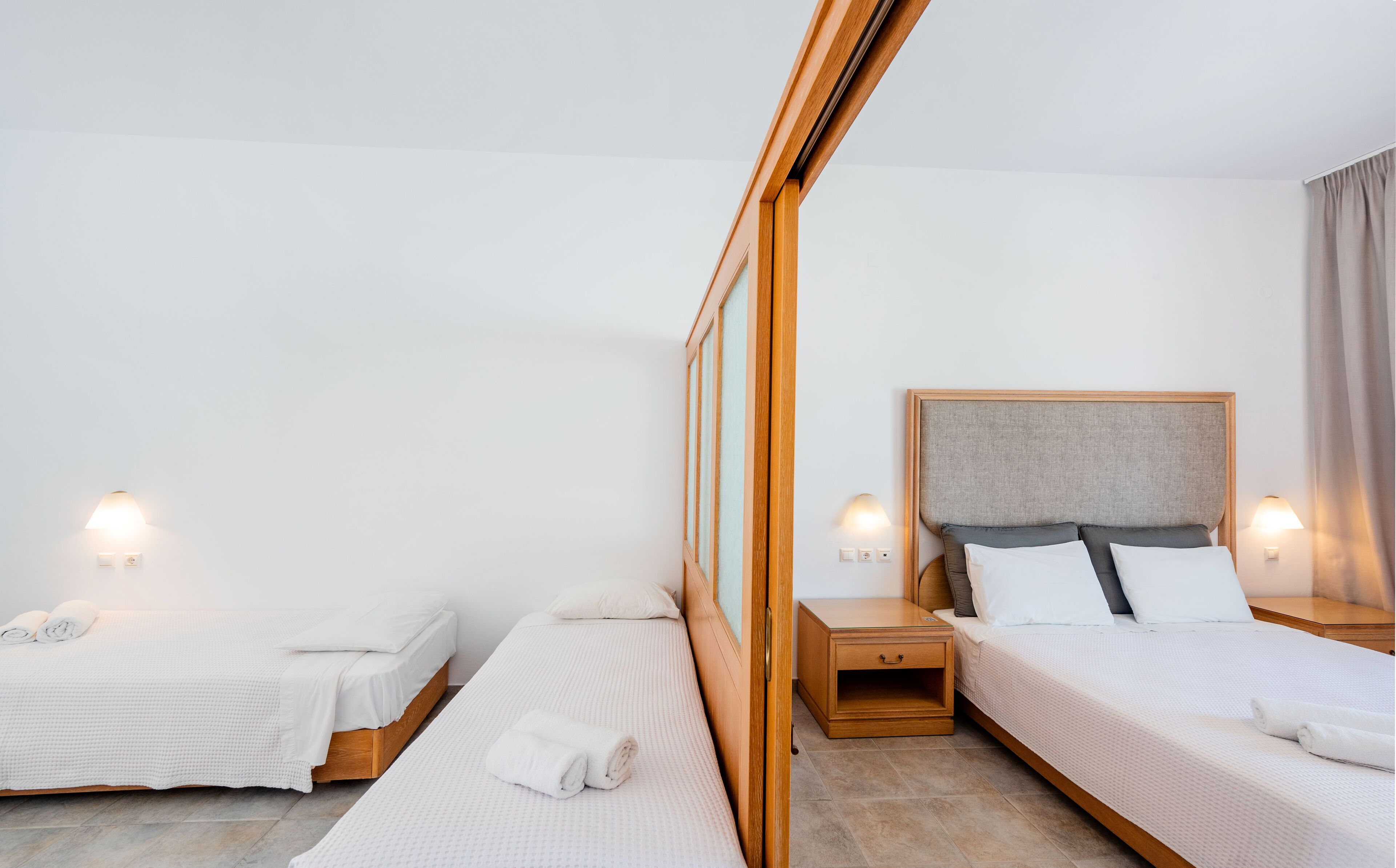 Habitación de hotel con dos camas, cada una con estructura de madera y ropa de cama blanca. Hay mesitas de noche con lámparas y un espejo grande en la pared.
