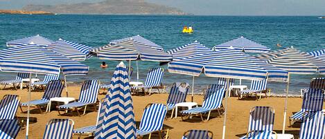 A beach with striped umbrellas and lounge chairs.