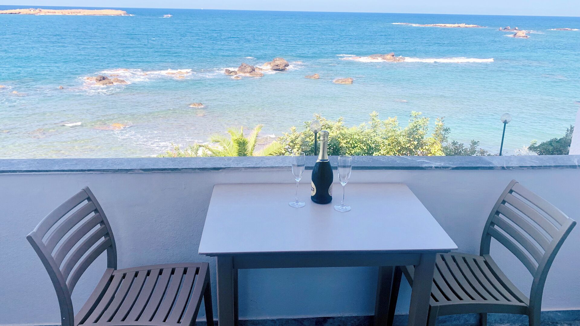 A table with two chairs and a bottle of champagne on a balcony overlooking the sea.