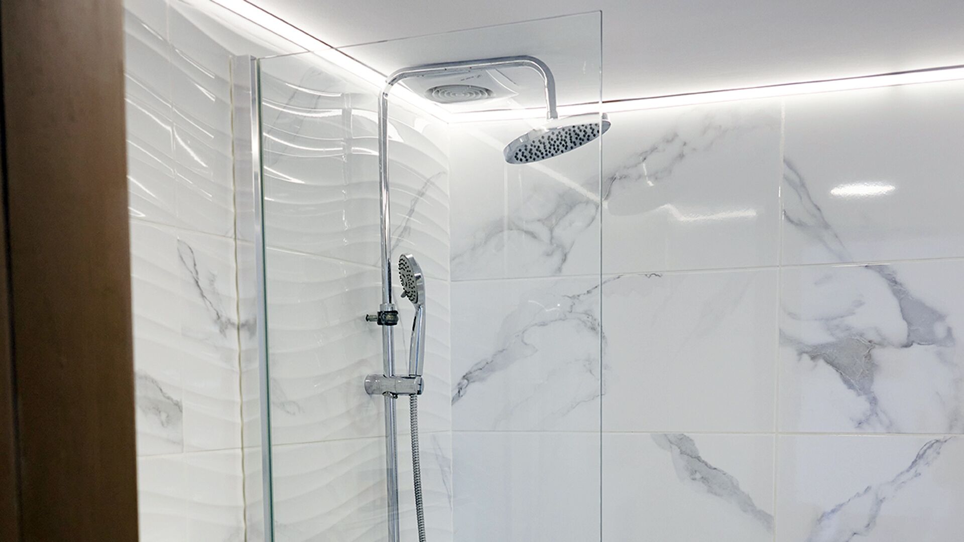 Ducha moderna con cabina de vidrio, cabezal de ducha de mano y un cabezal de ducha de lluvia empotrado.